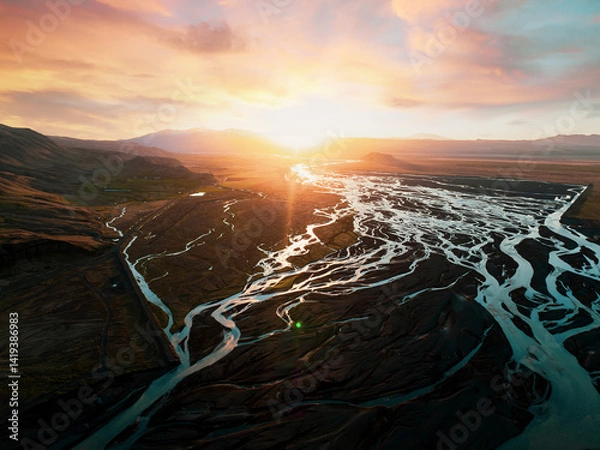 Obraz Golden sunset over a complex network of glacial rivers flowing across a dark Icelandic plain, with intense warm light and vibrant reflections on the water.