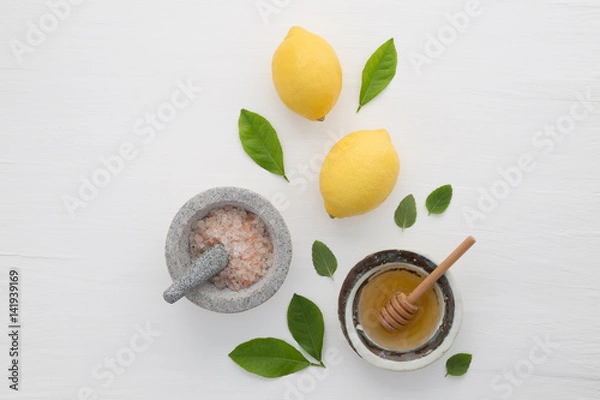 Fototapeta Homemade skincare concept, bath salt, lemon, honey dipper and mint on white wooden background from top view. Good for background and space.
