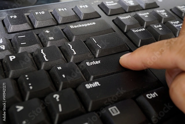 Fototapeta Close-up of a hand pressing the Enter key on a computer keyboard, showcasing the textured black surface and surrounding keys.