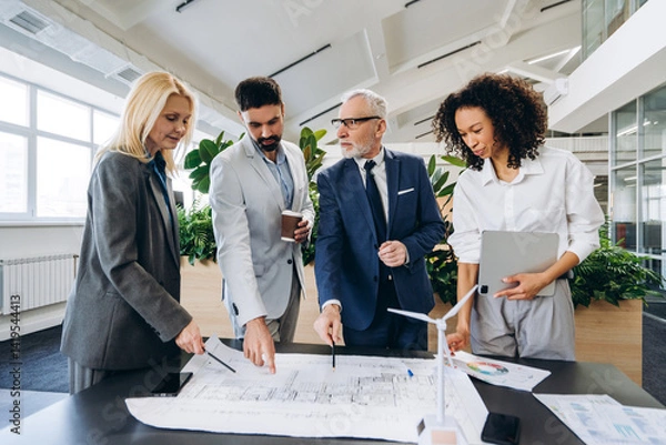 Fototapeta Engineers analyzing blueprint for sustainable building project, startup