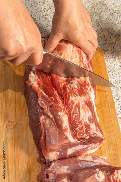 Obraz A cook's hand cuts raw pork neck with a knife for cooking. Close-up