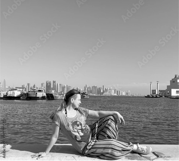Fototapeta Portrait of a 50-year-old woman in bright trousers sitting on a pier in Doha, Qatar