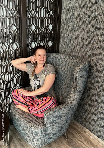Fototapeta portrait of a 50-year-old woman in bright trousers sitting in an armchair