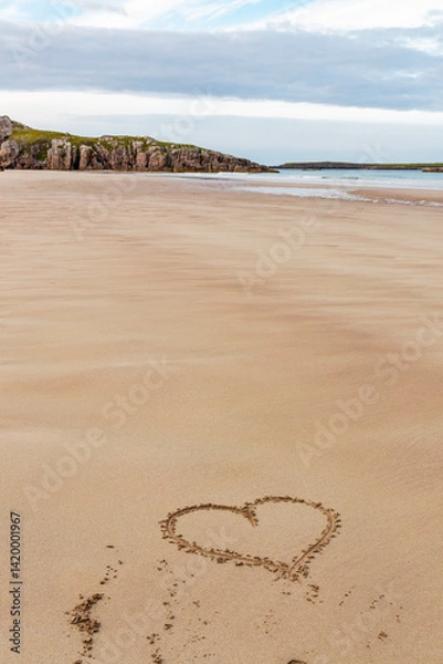 Fototapeta Ceannabeinne Beach shines under a clear summer sky. Crystal-clear waters, golden sand with a heart drawn on it, and lush green grass create a pristine and romantic coastal escape.

