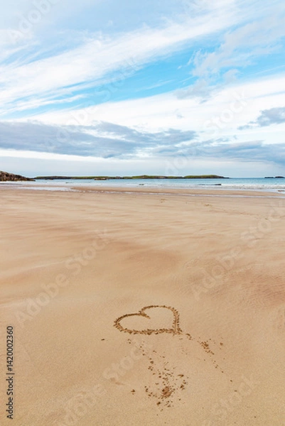 Fototapeta Ceannabeinne Beach shines under a clear summer sky. Crystal-clear waters, golden sand with a heart drawn on it, and lush green grass create a pristine and romantic coastal escape.

