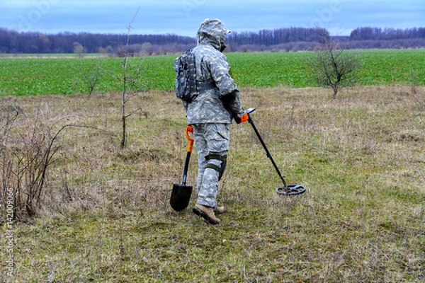Obraz Man with a device for finding treasures with a shovel on the field