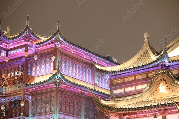 Fototapeta Colorful nighttime photo of Asian-style architecture. The building is decorated with pink, yellow, and purple lights on the ornate rooftop.