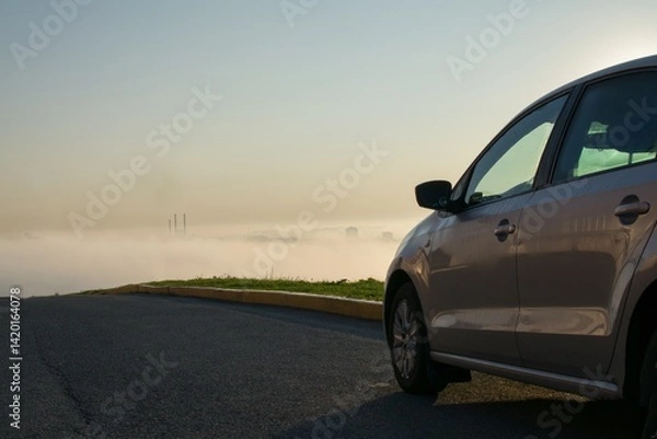 Fototapeta A clean, new car is parked on the side of the road on a mountain against the backdrop of a city in the fog