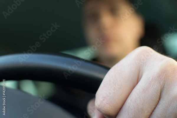 Fototapeta The driver's left hand holds the steering wheel against the background of a blurred face in the car interior