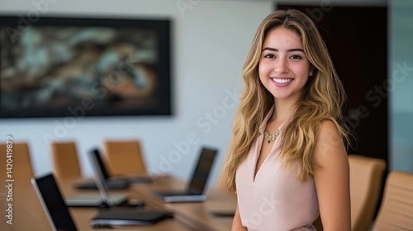 Fototapeta A woman in a gray blazer and cream turtleneck stands confidently in a modern conference room, smiling as she gestures while speaking.