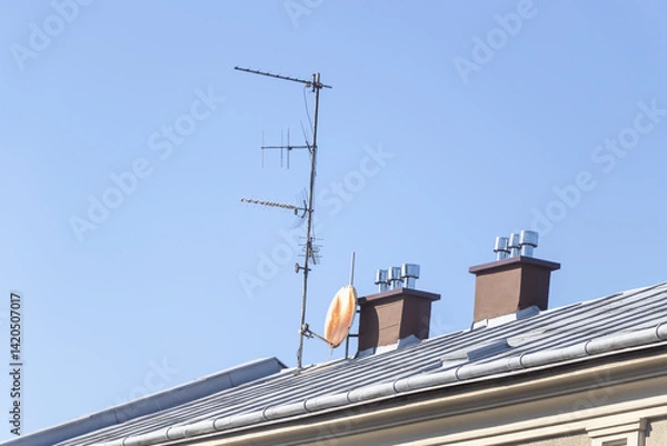 Obraz Communication antenna installed on a residential roof, featuring multiple chimneys against a clear blue sky. Represents technology in home settings.