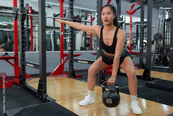 Fototapeta Concentrated sportswoman is doing kettlebell swing exercise to train her body inside a modern gym, demonstrating strength and dedication to healthy lifestyle