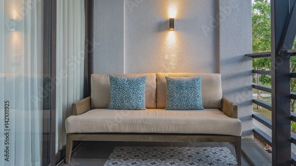 Fototapeta A place to relax on the balcony. A soft beige sofa with patterned cushions stands against the wall. The sconce is lit. Latticed railings. Tulle curtains on the windows. Tiled floor. Philippines.