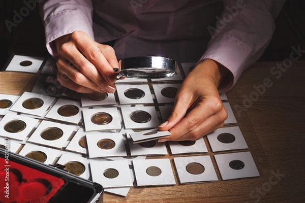 Fototapeta Old coin in the woman’s hand through the magnifying glass