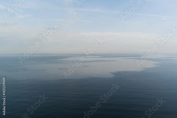Fototapeta Calm surface of the Baltic Sea off the coast of Estonia on a hazy day, with a solitary cargo ship on the distant horizon.
