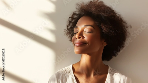Obraz A graceful woman in white closes her eyes and smiles softly as sunlight touches her face, capturing a sense of inner peace and mindful relaxation sunlit face, gentle smile, feminin