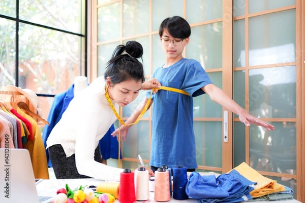 Fototapeta Asian women fashion designer  working and measure the customer in the showroom,  Lifestyle Stylish tailor clothing design and cutting cloths in studio.  Business small Concept.