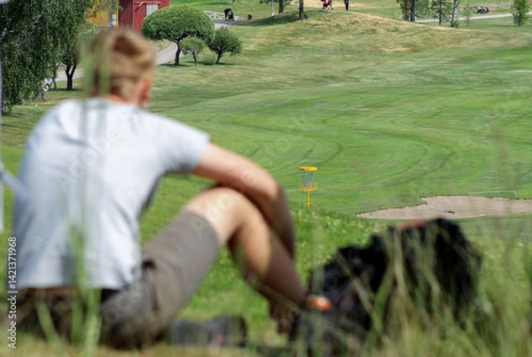 Obraz person is sitting on the hill and is following disc golf tournament