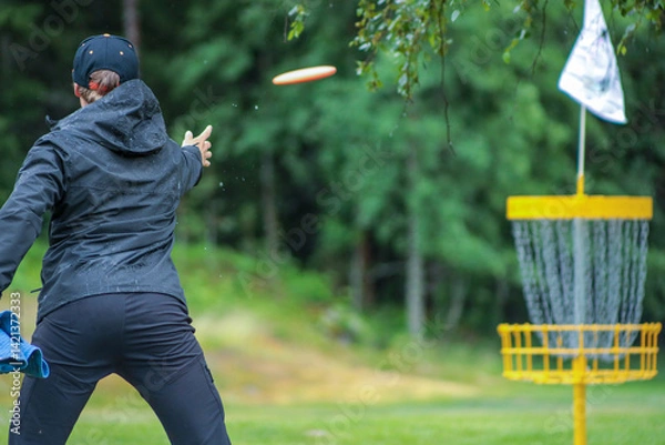 Obraz disc golf player putting to yellow basket in summer
