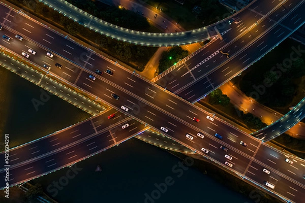 Fototapeta Aerial view of a busy road junction during nighttime with illuminated highways and moving vehicles.