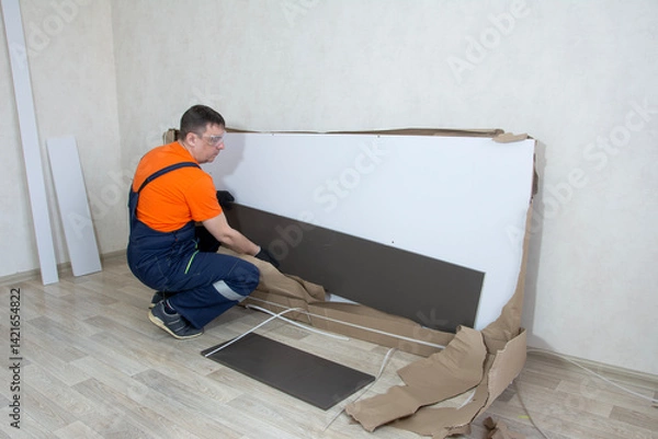Obraz A man in overalls collects furniture from a package in close-up in a bright room