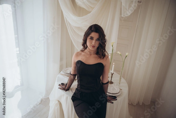 Fototapeta Woman in black dress leaning by the table with moody lighting