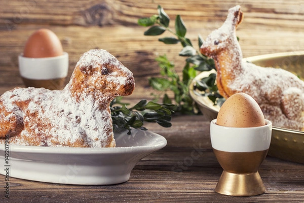 Obraz Eggs in a cups, lamb and rabbit easter cake on a wooden table