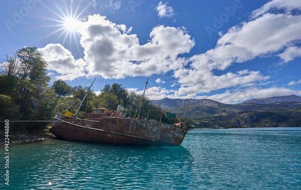 Fototapeta Abandoned ship in General Carrera Lake in Chile - remains of the closed mining industry. A ship located in a way of the boat tour to Marble Caves, attraction in the region. Rays radiating from the sun