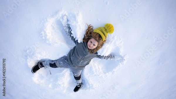 Fototapeta Winter fun. Child making a snow angel in winter day. Happy kid lying in the snow. Kid angel in snow. Winter kids with snowy angel wings. Smiling child on a winter day. Child in the snow lake angel.