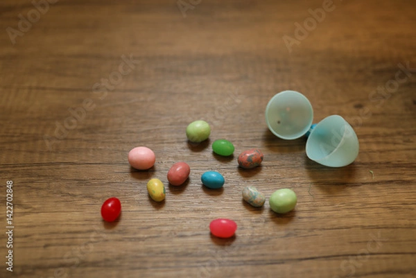 Fototapeta multi-colored jellybeans spilling out of the a light blue plastic Easter egg against a wood background with copy space available