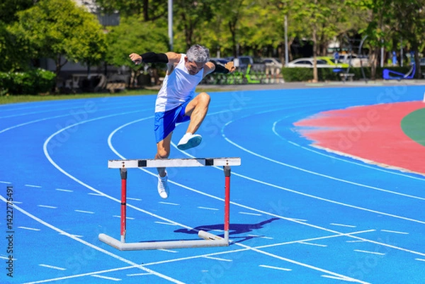 Obraz Senior Asian athlete is practicing hurdling running in the professional blue track for professional exercise, sport training workout and healthy for longevity