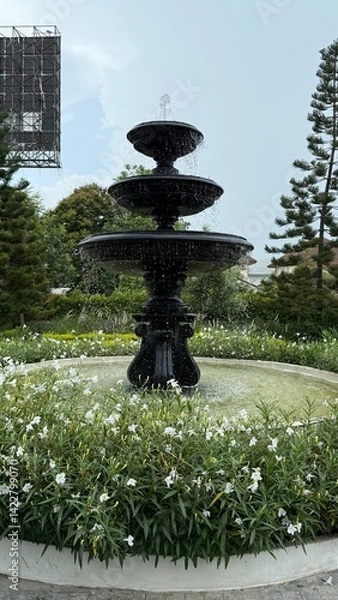 Fototapeta fountain in the garden,water flowing fountain decorating in flower garden,Streams of fountain water with sculpture statue with sun. Close-up of Garden waterfall in pond. Outdoor garden park.Relaxation