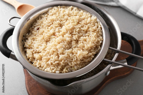 Fototapeta Colander with prepared brown rice in saucepan