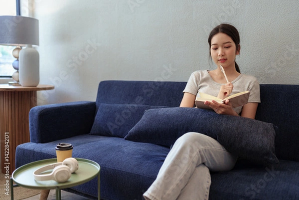 Obraz Calm young woman sitting on couch and writing in her diary during a peaceful moment in cozy home setting