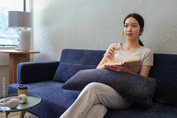 Obraz Calm young woman sitting on couch and writing in her diary during a peaceful moment in cozy home setting