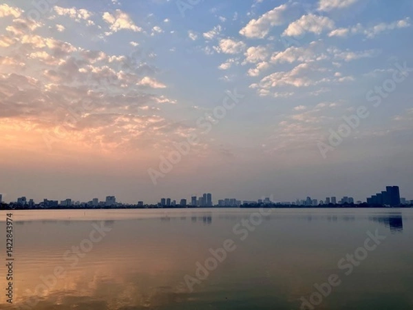 Fototapeta Misty Dawn Serenity: Urban Skyline Meets Gentle Cloud Formations on West Lake in Hanoi, Vietnam