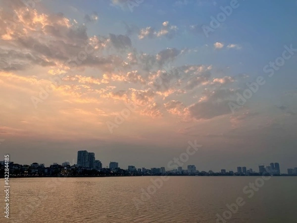 Fototapeta Pastel Dawn: Soft Urban Skyline Meets Gentle Cloud Formations on West Lake in Hanoi, Vietnam
