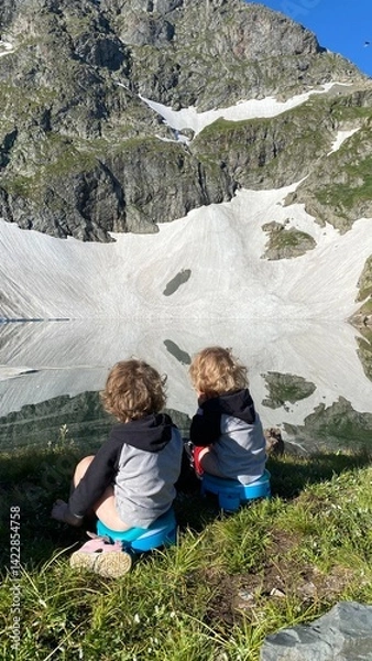 Fototapeta Children sit on potties on the shore of a lake in the mountains