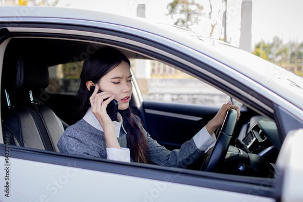 Fototapeta A woman is talking on the phone while driving.