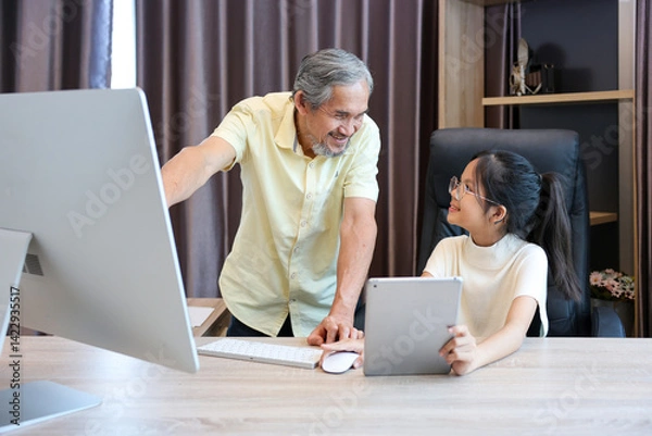 Obraz Young asian schoolgirl is doing her class homework assignment at home with advice from grandfather for education and study