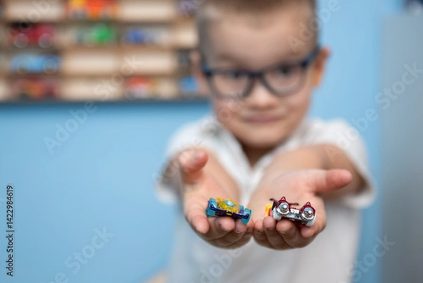 Fototapeta Boy with glasses holds a toy car in his hands in a playroom. Selective focus.