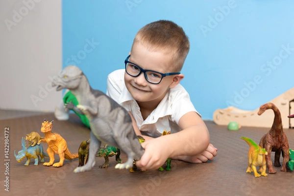 Fototapeta Boy enthusiastically plays with dinosaurs in his room, selective attention to his favorite toys, the concept of childhood and games.