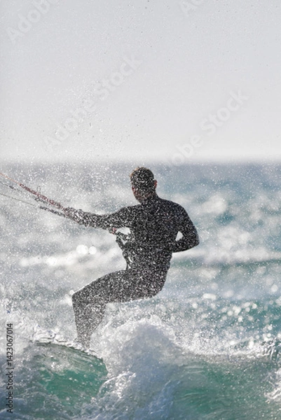 Fototapeta A dynamic photo capturing a kitesurfer in action, riding a wave while performing a maneuver. 