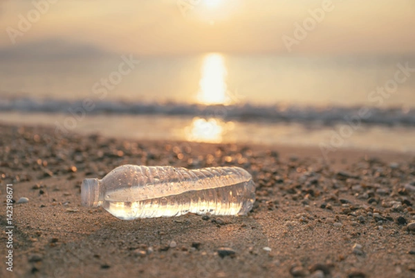 Obraz Plastic water bottle at sandy beach shoreline in summer morning, plastic pollution of ocean and seaside