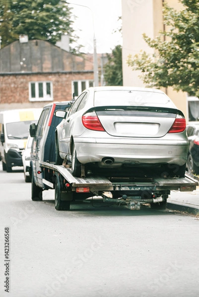 Fototapeta Tow truck transporting broken car in urban area