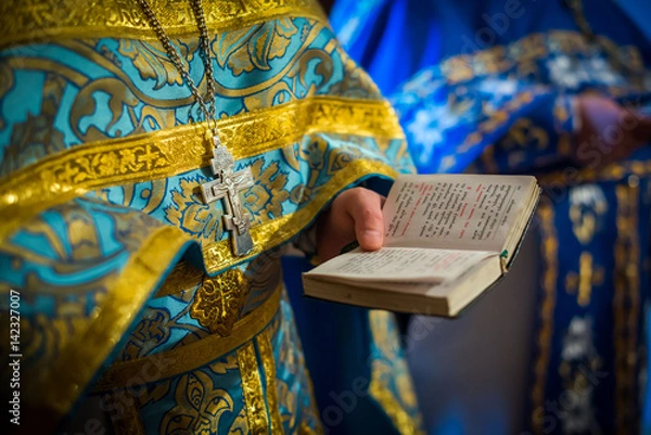 Fototapeta The clergyman reads the Bible, the Bible is in the hands of the priest, the priest is in the Orthodox Christian temple, the Bible in his hands
