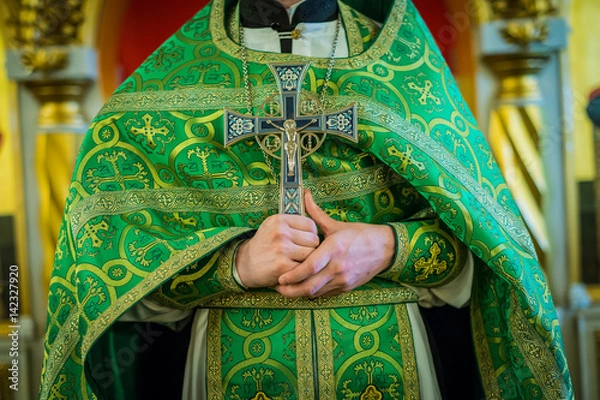 Fototapeta A priest in green vestments holds a large cross at his chest