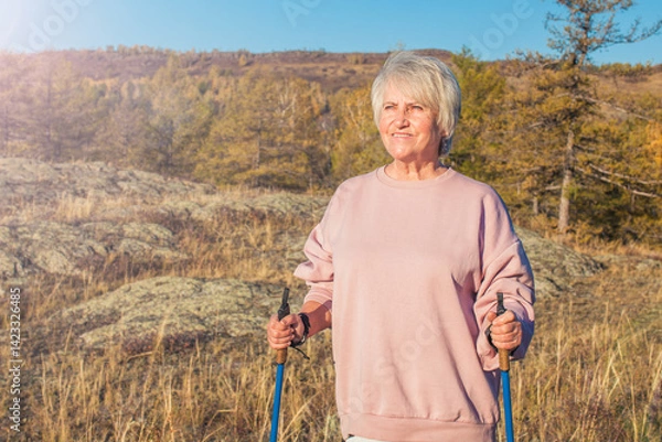Obraz Attractive short haired middle aged woman in activewear hiking in forest using poles for nordic walking