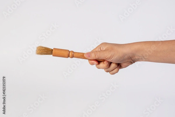 Fototapeta Hand using a wood little paintbrush isolated on a white background