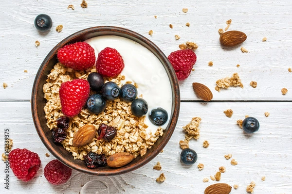 Obraz miska muesli owsianej z jogurtem, świeżymi malinami, jagodami i orzechami
